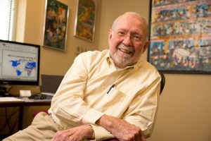 Public health leader seated in an office, smiling, with global health maps and artwork displayed in the background